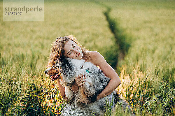 Young woman enjoying with her dog in a green rye field