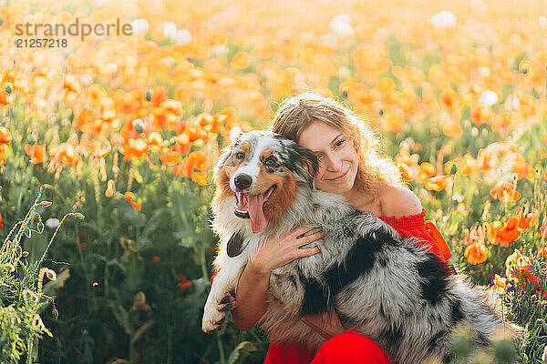 In vibrant poppy field under the warm sun  young woman with her dog