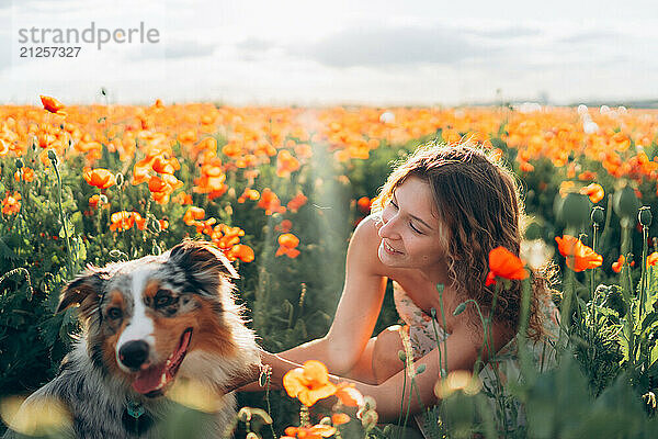 woman and her australian shepherd dog frolic in a vibrant poppy field