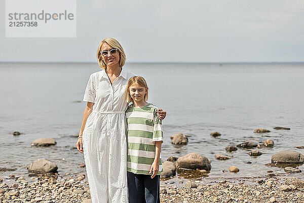 Embracing woman and daughter walking together on stony beach