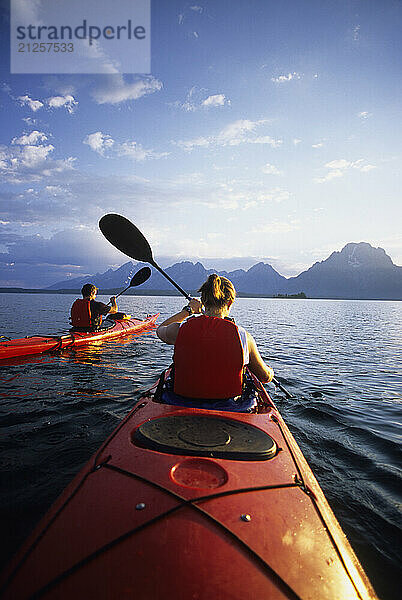 A young couple paddles sea kayaks across Jackson Lake on a sunny day in Grand Teton National Park  Jackson Hole  Wyoming (POV).