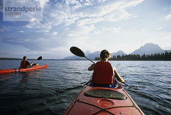 A young couple paddles sea kayaks across Jackson Lake on a sunny day in Grand Teton National Park  Jackson Hole  Wyoming (POV).