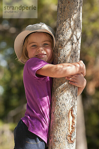 A preschool aged girl hugs a tree in Grand Teton National Park  Jackson Hole  Wyoming.