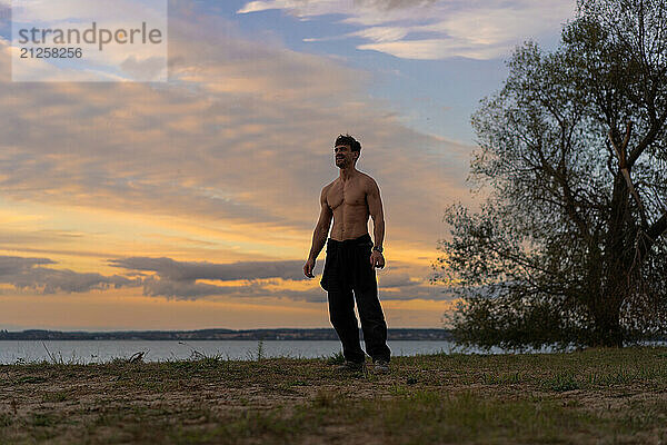 A man against the backdrop of the sunset sky on the shore of a lake.