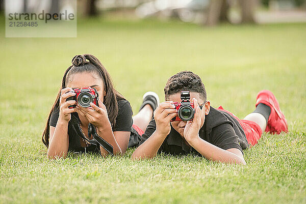 Boy and girl laying in the grass taking photos with their cameras