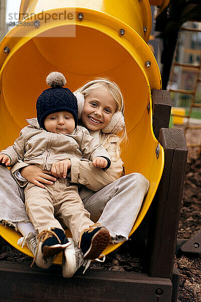 Sister is going down the slide with her little brother