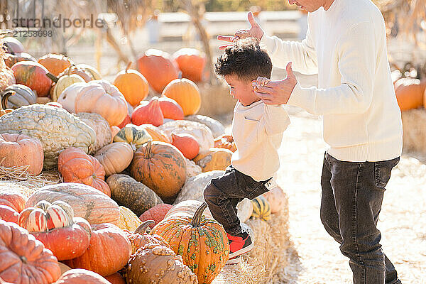 Father helping son up hay stacks and pumpkins