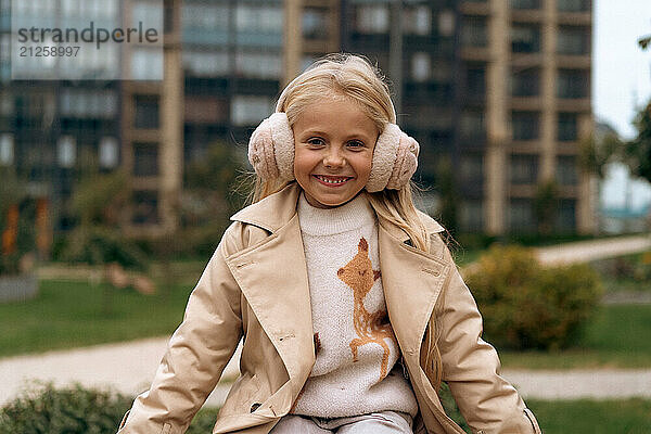 A little girl with long blond hair smiles in warm headphones