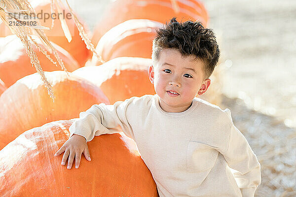 Little boy leaning against a big pumpkin