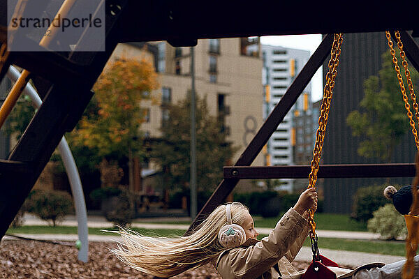 Cheerful girl playing on swing at park during autumn