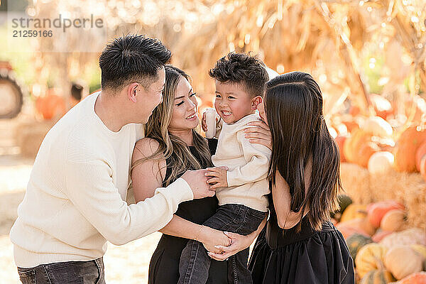 Family of four laughing in the middle of a pumpkin patch together