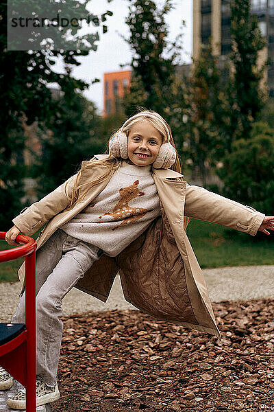 Cheerful girl playing on swing at park during autumn