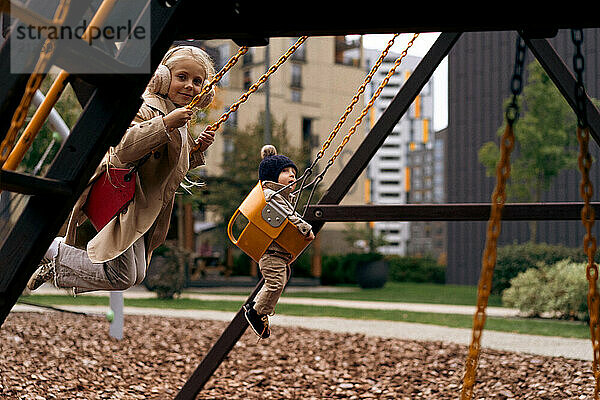 Brother and sister play on the swings at playground