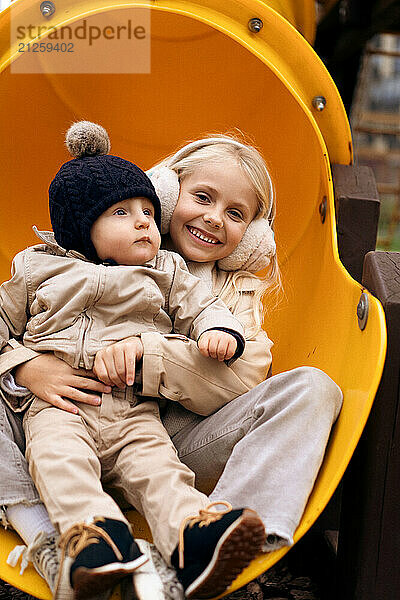 Sister is going down the slide with her little brother