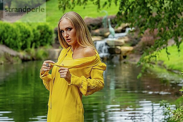 Blonde Schönheit glänzt in atemberaubender Herbstkleidung in der Nähe eines Wasserfalls im Park  eine malerische Herbstszene