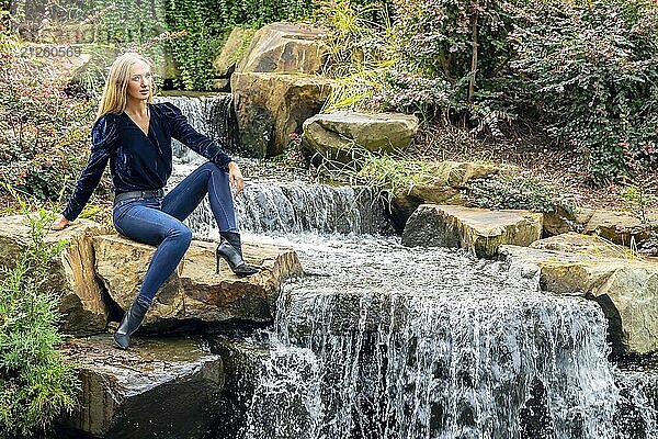 Blonde Schönheit glänzt in atemberaubender Herbstkleidung in der Nähe eines Wasserfalls im Park  eine malerische Herbstszene