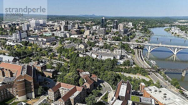 Ein Luftbild von Knoxville  Tennessee  zeigt ein lebendiges Stadtbild mit einer Mischung aus historischen und modernen Gebäuden  dem Tennessee River  der sich durch die Innenstadt schlängelt  üppigen grünen Parks und den fernen Smoky Mountains am Horizont