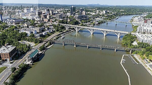 Ein Luftbild von Knoxville  Tennessee  zeigt ein lebendiges Stadtbild mit einer Mischung aus historischen und modernen Gebäuden  dem Tennessee River  der sich durch die Innenstadt schlängelt  üppigen grünen Parks und den fernen Smoky Mountains am Horizont