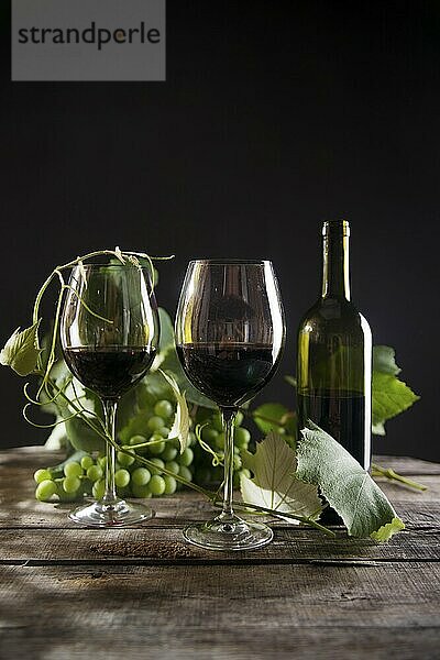 Glas Rotwein mit Flasche und Traube von sauren Trauben auf einem schwarzen Hintergrund