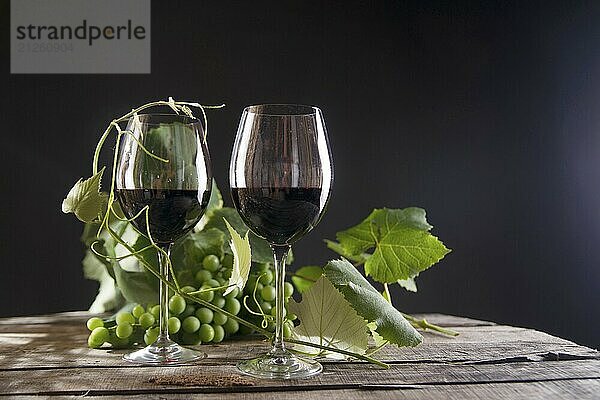 Glas Rotwein mit Flasche und Traube von sauren Trauben auf einem schwarzen Hintergrund