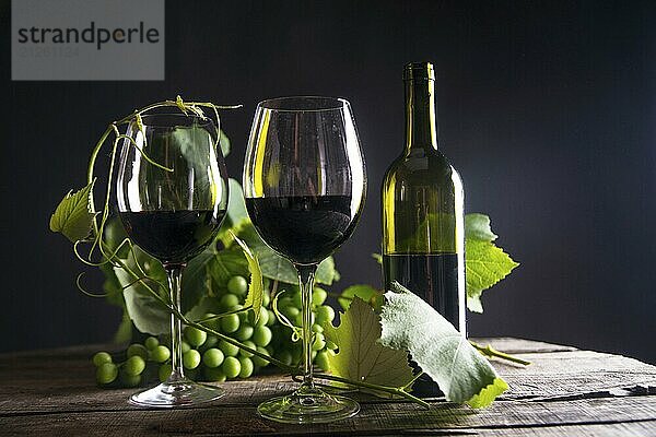 Glas Rotwein mit Flasche und Traube von sauren Trauben auf einem schwarzen Hintergrund