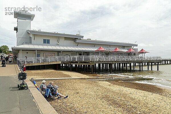 Menschen sitzen am Strand neben dem Pier Gebäude  Felixstowe  Suffolk  England  UK