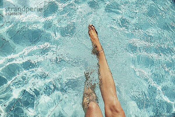 Schöne Beine einer Frau plantschen im türkisfarbenen Pool