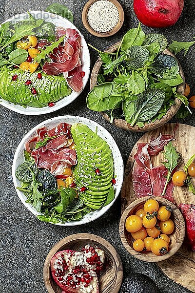 Lebensmittel  Low Carbs Schüssel Frischer Salat mit grünem Spinat  Rucola  Avocado und Serrano Schinken in weißer Schüssel  grauer Hintergrund  Draufsicht