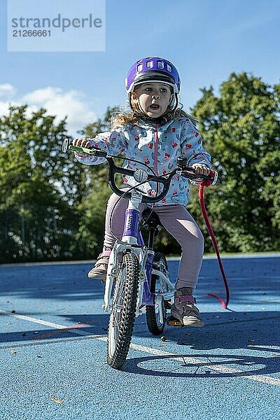 Mädchen mit lila Helm fährt lächelnd Fahrrad auf sonnigem Sportplatz