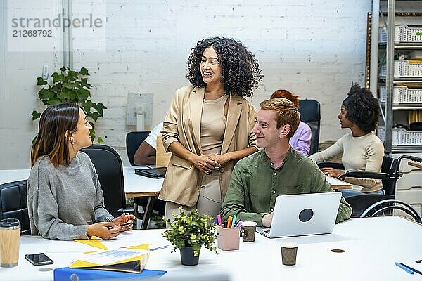 Drei verschiedene weibliche und männliche Mitarbeiter unterhalten sich abgelenkt in einem modernen Coworking Raum