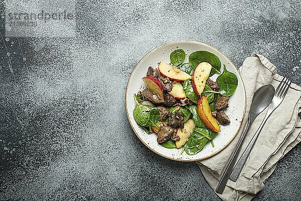 Gesunder Salat mit eisenreichen Zutaten Hühnerleber  Äpfel  frischer Spinat und Walnüsse auf weißem Keramikteller  grauer rustikaler Steinhintergrund Draufsicht Kopierraum  Foodfotografie  food photography  food photography