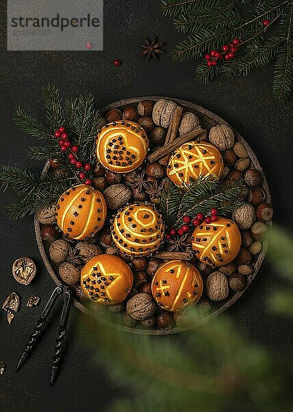 Weihnachtliche Dekoration aus Orangen und Nelken mit verschiedenen Motiven  umgeben von Nüssen und Tannenzweigen auf einem dunklen Hintergrund. Handgemachte Dekoration für Weihnachten