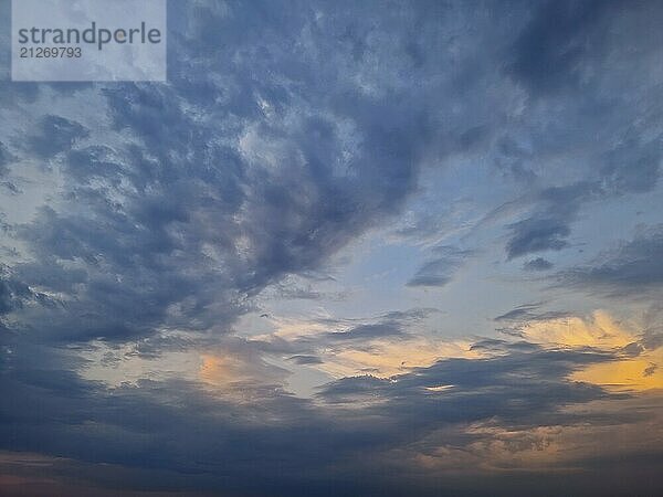 Eine weite Himmelsansicht mit dynamischen Wolkenformationen  Blautönen und zartem Orange am Horizont  die entweder einen Sonnenaufgang oder einen Sonnenuntergang suggerieren. Das Zusammenspiel von Licht und Wolkenlandschaft schafft eine heitere Atmosphäre