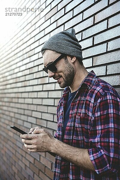 Hipster sms texting Telefon App in der Stadt Straße auf Backsteinmauer Hintergrund. Amazing Mann hält Smartphone in smart casual wear stehen. Urban junge professionelle Lebensstil