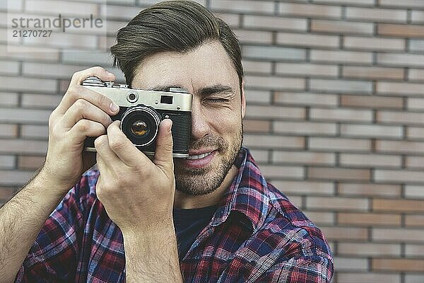 Mann mit Retro Fotokamera Mode Reisen Lifestyle im Freien  während stehend gegen Backsteinmauer Hintergrund