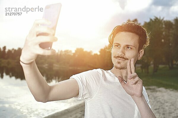 Porträt des jungen gut aussehend stilvoll lächelnd Kerl macht selfie gegen den See. schöne Natur