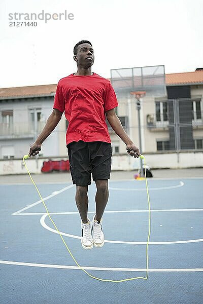 Vertikales Foto eines sportlichen afrikanischen jungen Basketballspielers  der zum Aufwärmen Seil springt