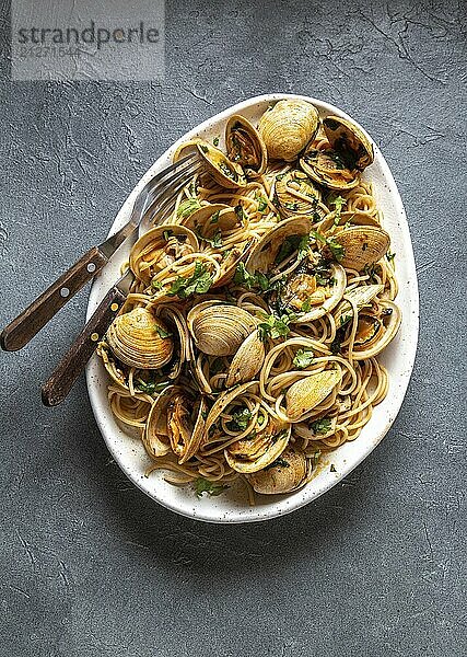 Lebensmittel  Meeresfrüchte Pasta. ITALIENISCHE SPAGHETTI ALLE VONGOLE. Venusmuscheln Spaghetti auf weißem Teller mit Weißwein  grauer Hintergrund. Ansicht von oben