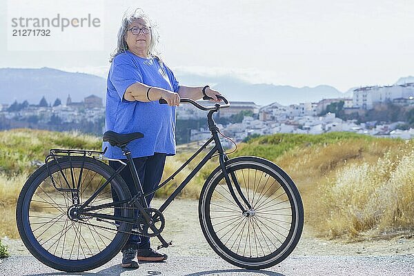 Übergewichtige weißhaarige ältere Frau auf einem Fahrrad im Retro Stil mit einer Stadt im Hintergrund