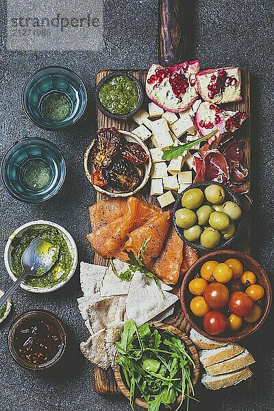 Lebensmittel  Antipasto. Wein Set Vorspeise. Schinken Serrano  geräucherter Lachs  getrocknete und frische Tomaten  Olivenkäse  Wein an Bord. Ansicht von oben  grauer Hintergrund aus Beton