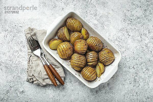 Hasselback Kartoffeln mit Kräutern in weißer Keramik Auflaufform auf weißem Beton Tisch Hintergrund von oben. Leckere hausgemachte Akkordeon Backkartoffeln zum Abendessen  Food Fotografie