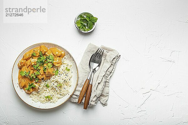 Traditionelles indisches Gericht Hühnercurry mit Basmatireis und frischem Koriander auf rustikalem weißen Teller auf weißem Betontisch Hintergrund von oben. Indisches Abendessen  Platz für Text  Food Fotografie  food photography  food photography