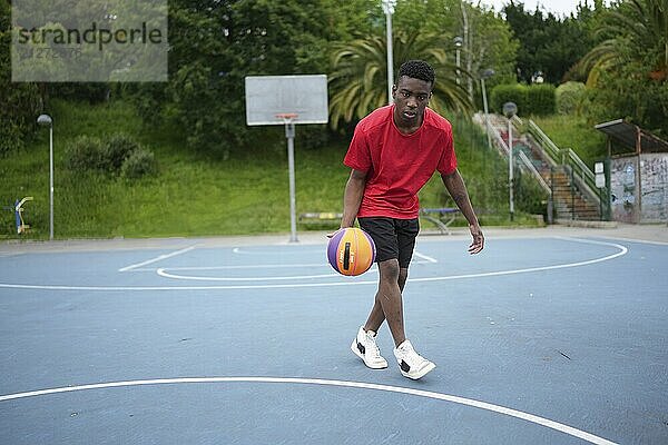 Foto in voller Länge von Dribbelübungen eines afrikanischen Mannes auf einem Basketballplatz im Freien