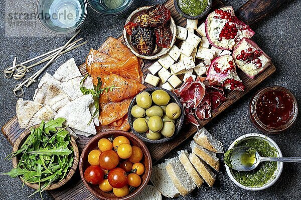 Lebensmittel  Antipasto. Wein Set Vorspeise. Schinken Serrano  geräucherter Lachs  getrocknete und frische Tomaten  Olivenkäse  Wein an Bord. Ansicht von oben  grauer Hintergrund aus Beton