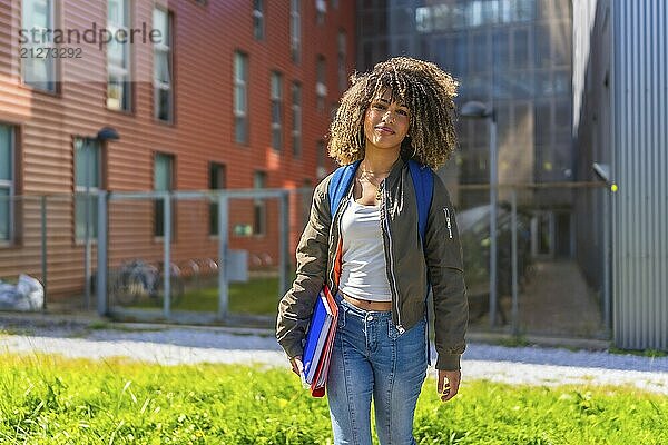 Schöne Lateinstudentin  die vor der Universität steht  in die Kamera lächelt und Mappen  Notizbücher und einen Rucksack trägt