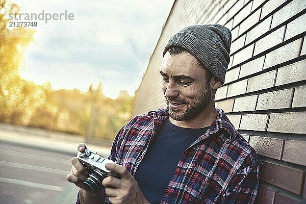 Lächelnder Mann mit Retro Fotoapparat Mode Reisen Lifestyle im Freien  während gegen Backsteinmauer Hintergrund stehen