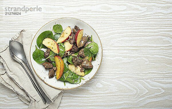 Gesunder Salat mit eisenreichen Zutaten Hühnerleber  Äpfeln  frischem Spinat und Walnüssen auf weißem Keramikteller  weißer Holzhintergrund von oben Platz für Text  Foodfotografie