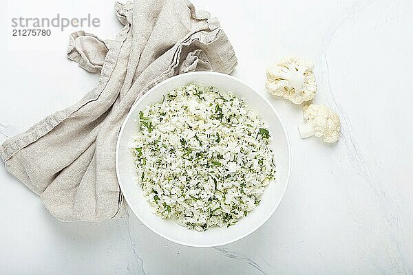 Roher Blumenkohlreis oder Couscous mit Dill in weißer Schale  gesunde kohlenhydratarme Gemüsebeilage für Keto Diät und gesunde kalorienarme Ernährung auf weißem Marmor Hintergrund  Food Fotografie