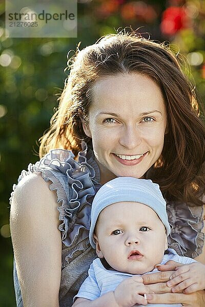 Porträt einer jungen glücklichen Frau und eines Babys in einem Garten vor einem Hintergrund mit Frühlingsblumen