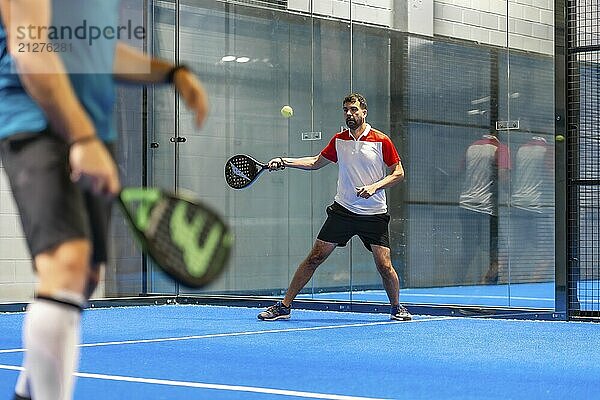 Zwei reife männliche Freunde spielen Paddle Tennis in einem blauen Innenplatz